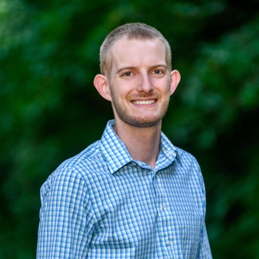 A headshot of Tim. He's wearing a collared blue shirt with a plaid pattern.